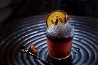 a cocktail with ice and orange slices on a black plate