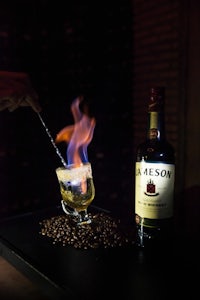 a person is pouring a drink into a glass with a flame