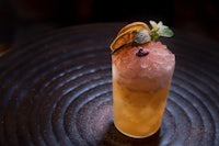 a cocktail with ice and mint sitting on top of a black plate
